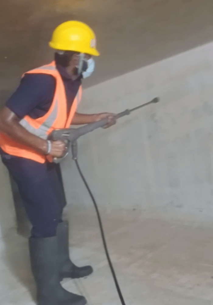 A man wearing glouse, mask and helmet and cleaning water tank with pressure wash